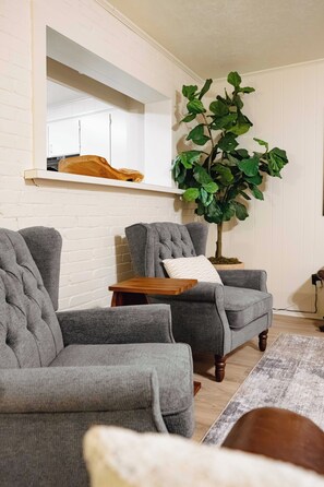 A living room with two grey sofas, a wooden coffee table, and a large green plant. - Spacious 4-bedroom house in Historic College Station near TAMU (College Station)