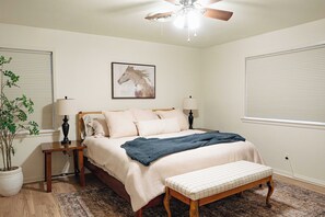A bedroom with a bed, bedside tables, a ceiling fan, a wall-mounted painting, and a potted plant. - Spacious 4-bedroom house in Historic College Station near TAMU (College Station)