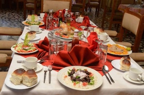 Une table à manger dressée avec différents plats, notamment un poulet rôti, des salades et des petits pains.