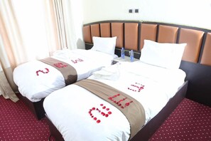 Une chambre d’hôtel avec deux lits, une tête de lit marron et une moquette rouge.
