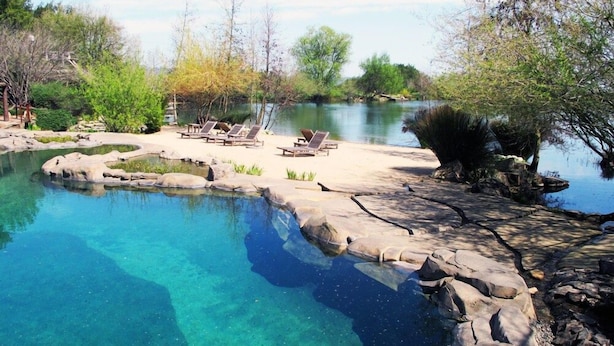 A clear pool with rocks and lounge chairs, surrounded by trees and a natural landscape. - Dib Anbessa Hotel (Bahir Dar)