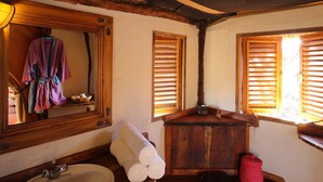A rustic bathroom with a wooden vanity, a sink, a mirror, and wooden shutters on the windows. - Lewa Safari Camp (Meru)