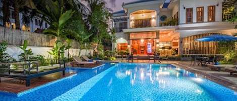 A swimming pool with lounge chairs, a bar area, and a two-story building with a balcony.
