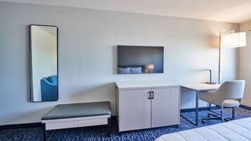 Ein Hotelzimmer mit einem Bett, einem Schreibtisch, einem Sessel, einer Bank, einem Schrank, einem Spiegel und einer Wandleuchte.