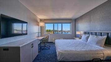 Quarto de hotel com cama, escrivaninha, cadeira, televisão e janela com vista.