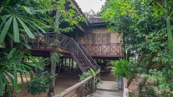 A wooden structure with a staircase leading to a covered area, surrounded by dense foliage.