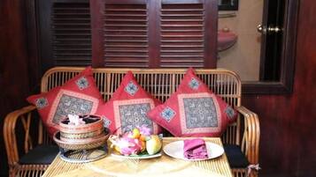 A wicker sofa with red cushions, a woven table with a fruit bowl, a plate, and a folded napkin.