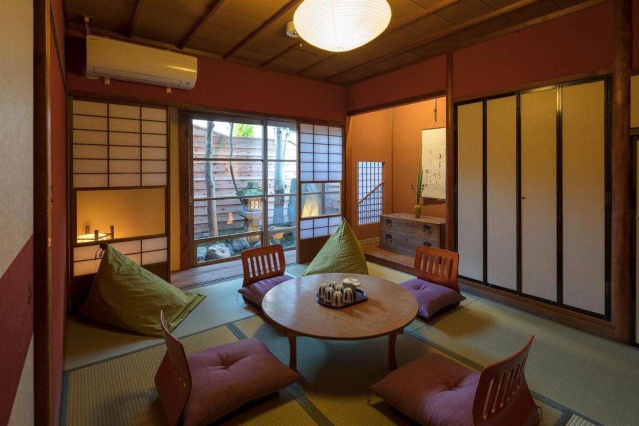A traditional Japanese room with tatami flooring, a low table with cushions, sliding doors, and a view of the outside.