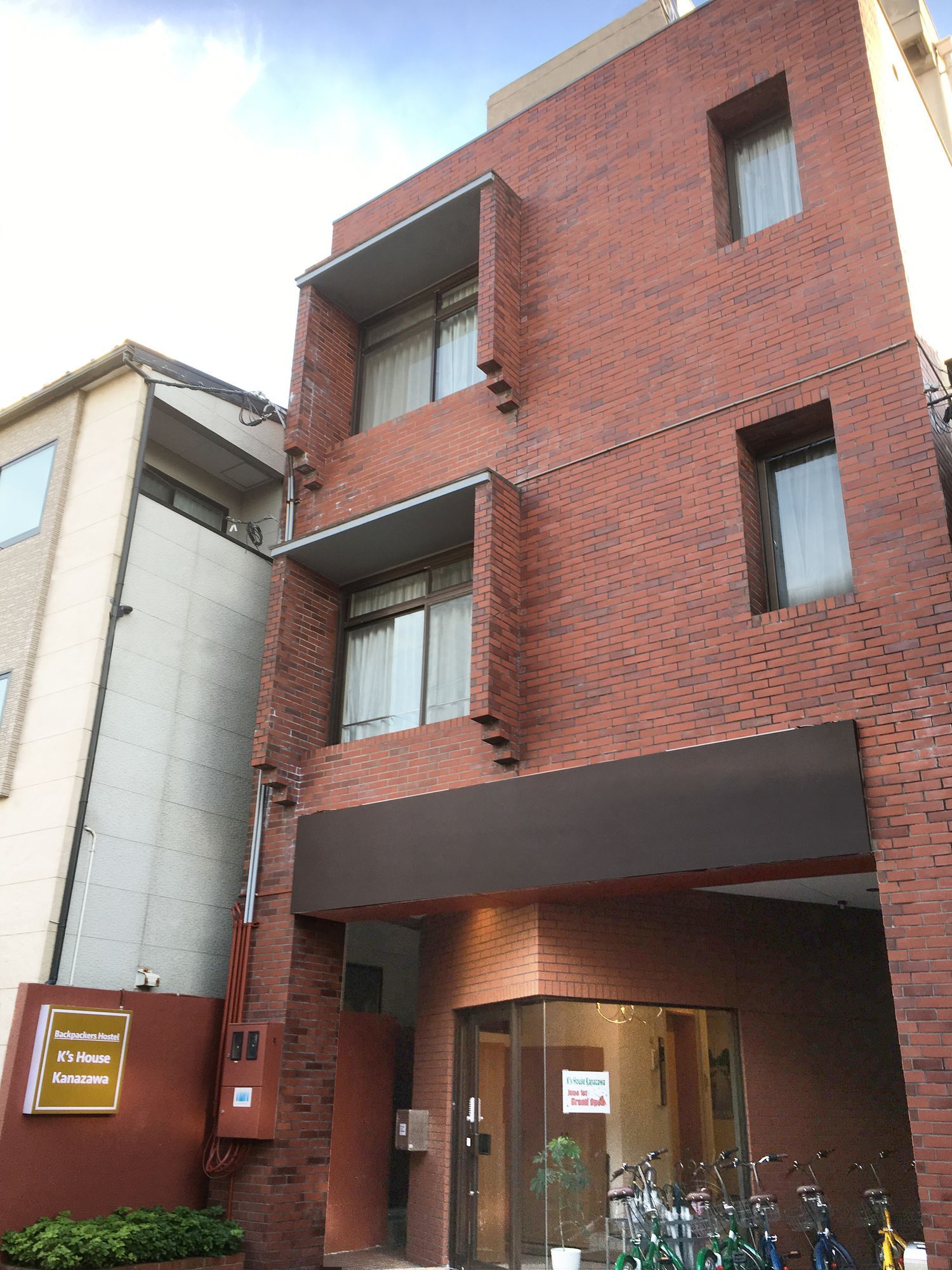 Un edificio de varios pisos con fachada de ladrillo, entrada a nivel de calle con puerta de vidrio y un letrero que indica que es un albergue juvenil.