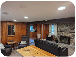A cozy living room with a fireplace, wooden walls, and a dining area.