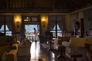 A cozy lounge area with a wooden ceiling, large windows, and a view of the outdoors.