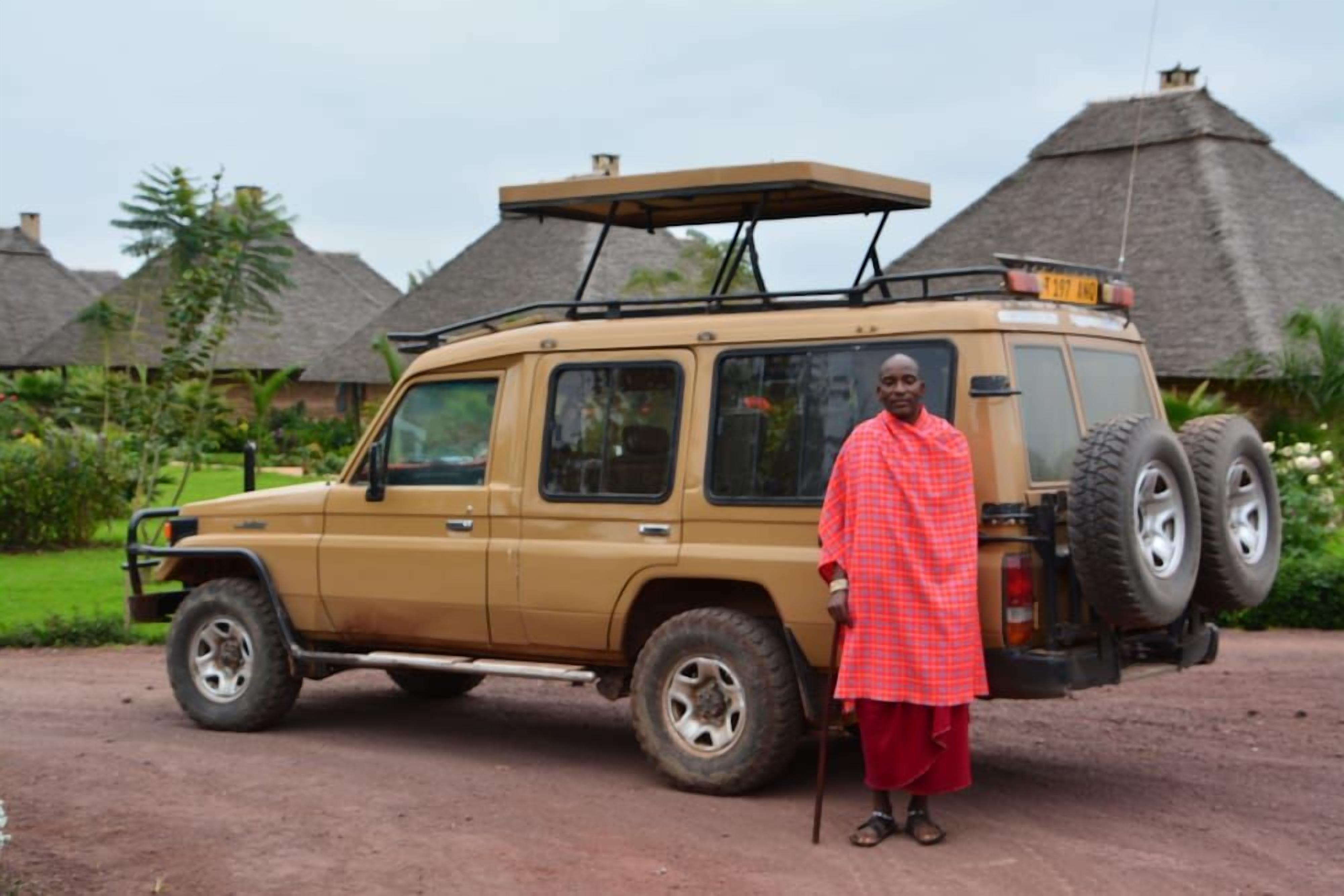 A vehicle parked on a dirt road with thatched-roof huts in the background.