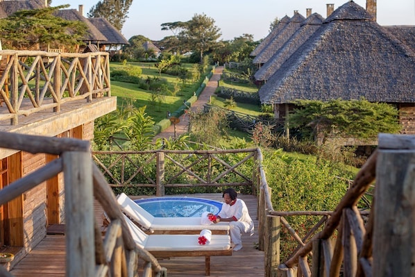 A wooden deck with a hot tub, lounge chairs, and a person in traditional attire. - Neptune Ngorongoro Luxury Lodge - All Inclusive (Karatu)