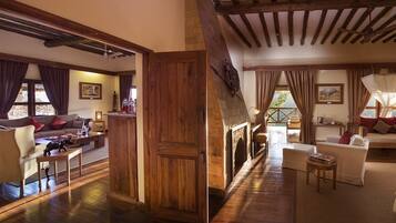 A spacious living area with a fireplace, wooden beams, and a view through large windows.