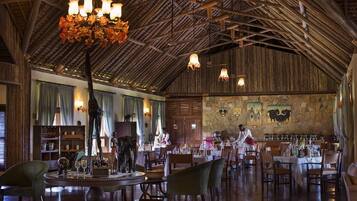 A spacious dining area with high ceilings and exposed wooden beams, featuring a central chandelier and multiple hanging light fixtures.