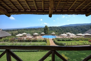 Zona de piscina amb ombrel·les i seients, envoltada de vegetació exuberant i muntanyes al fons.