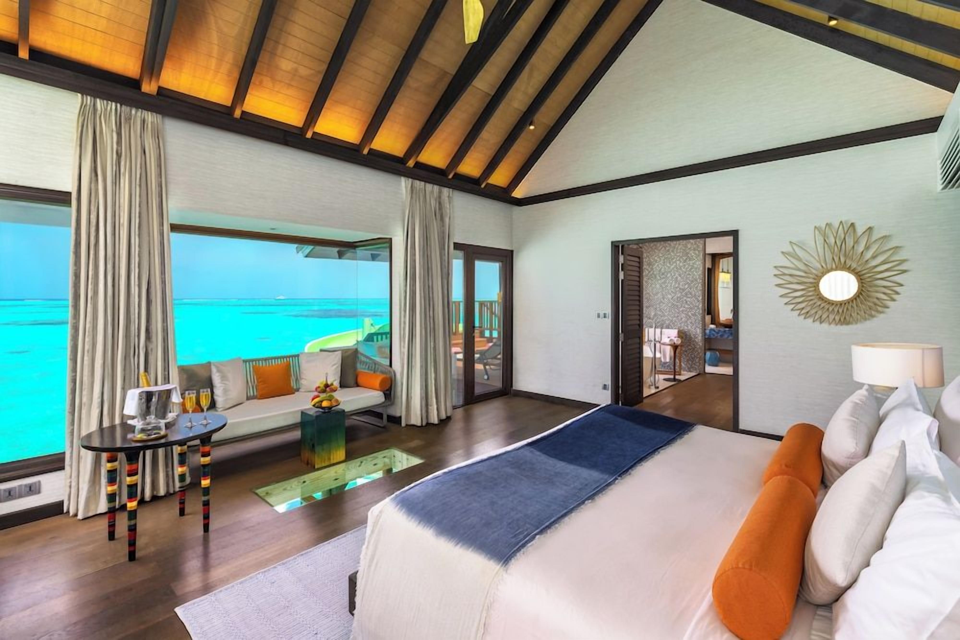Habitación de hotel con una cama grande, un sofá, una mesa con lámpara y vista al océano.
