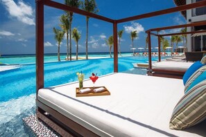 A hotel room with a bed, a tray with towels and a drink, and a view of a pool and beach. - Ozen Life Maadhoo Resort (Maadhoo)