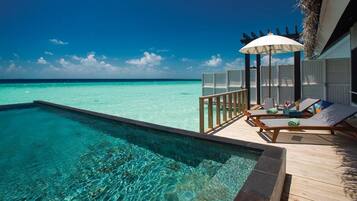 An infinity pool with clear turquoise water, a wooden deck, lounge chairs, and an umbrella.