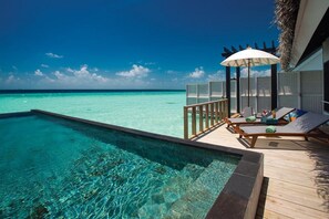 Una piscina infinita con agua turquesa cristalina, una terraza de madera, sillas de descanso y una sombrilla.