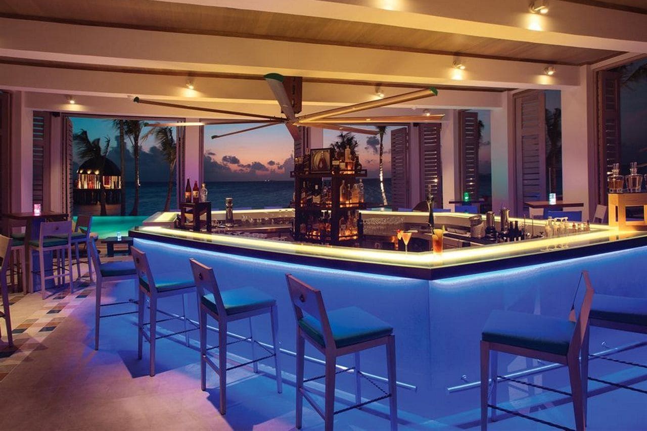 Zona de bar con piscina, taburetes y vistas al océano.