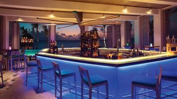 Zona de bar con piscina, taburetes y vistas al océano.
