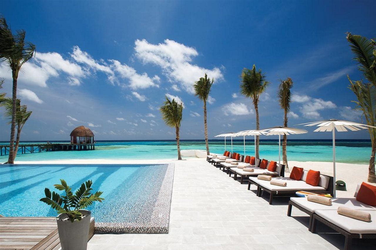 A poolside area with lounge chairs and umbrellas, a wooden deck, and a view of the ocean.