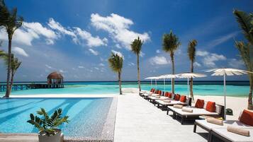 A poolside area with lounge chairs and umbrellas, a wooden deck, and a view of the ocean.