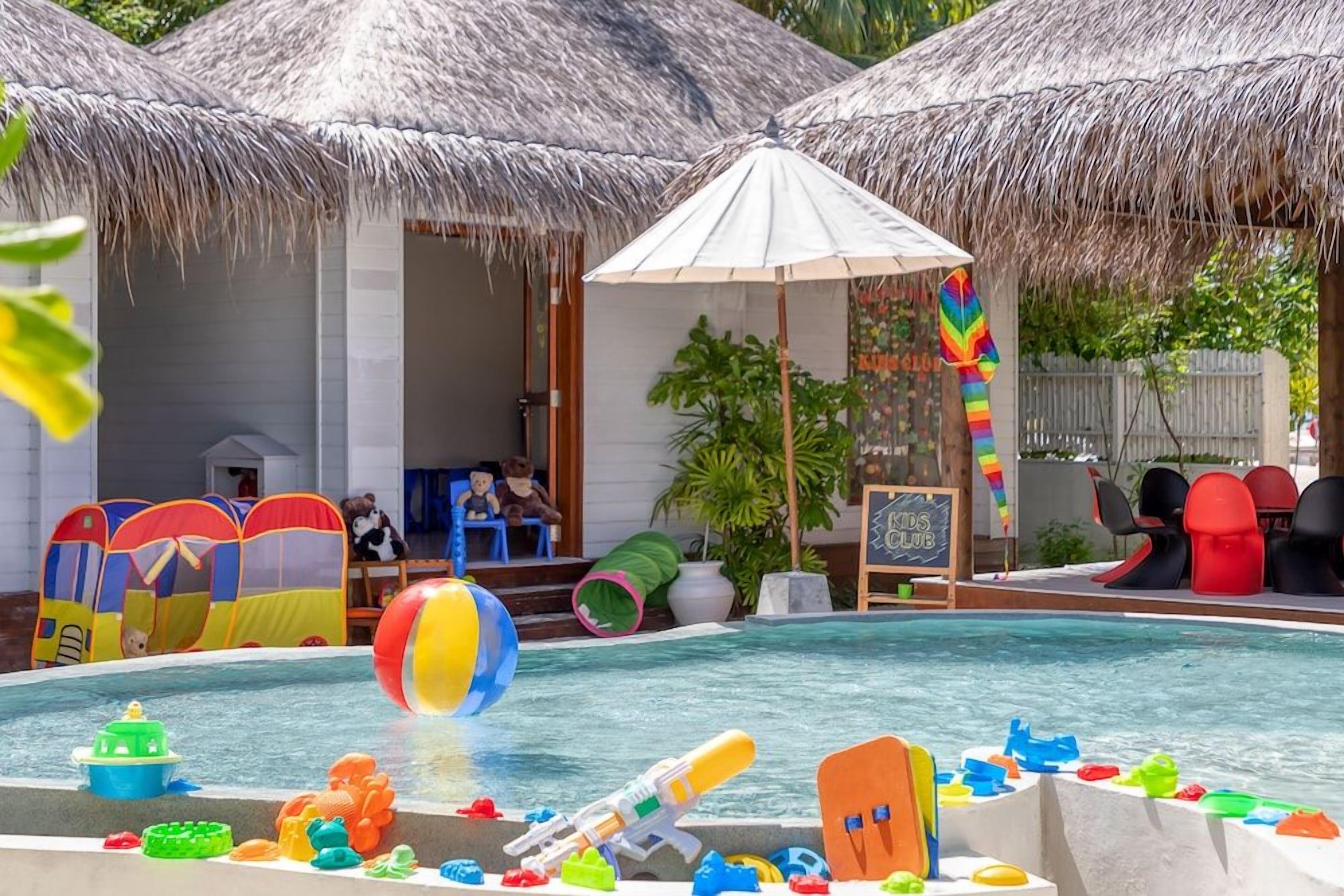 A pool area with a water slide, inflatable toys, and a children's club sign.
