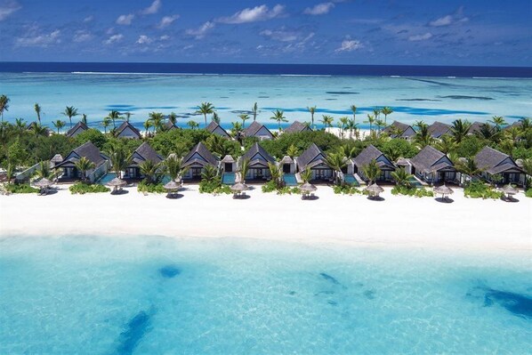 Un resort frente al mar con bungalows sobre el agua, aguas turquesas cristalinas y una playa de arena blanca.