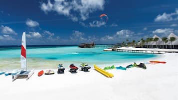 A beach with a clear blue sky, a pier, and overwater bungalows.