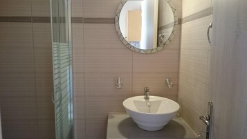Un baño con cabina de ducha de vidrio, un espejo redondo con marco decorativo y un lavabo blanco con grifo moderno.