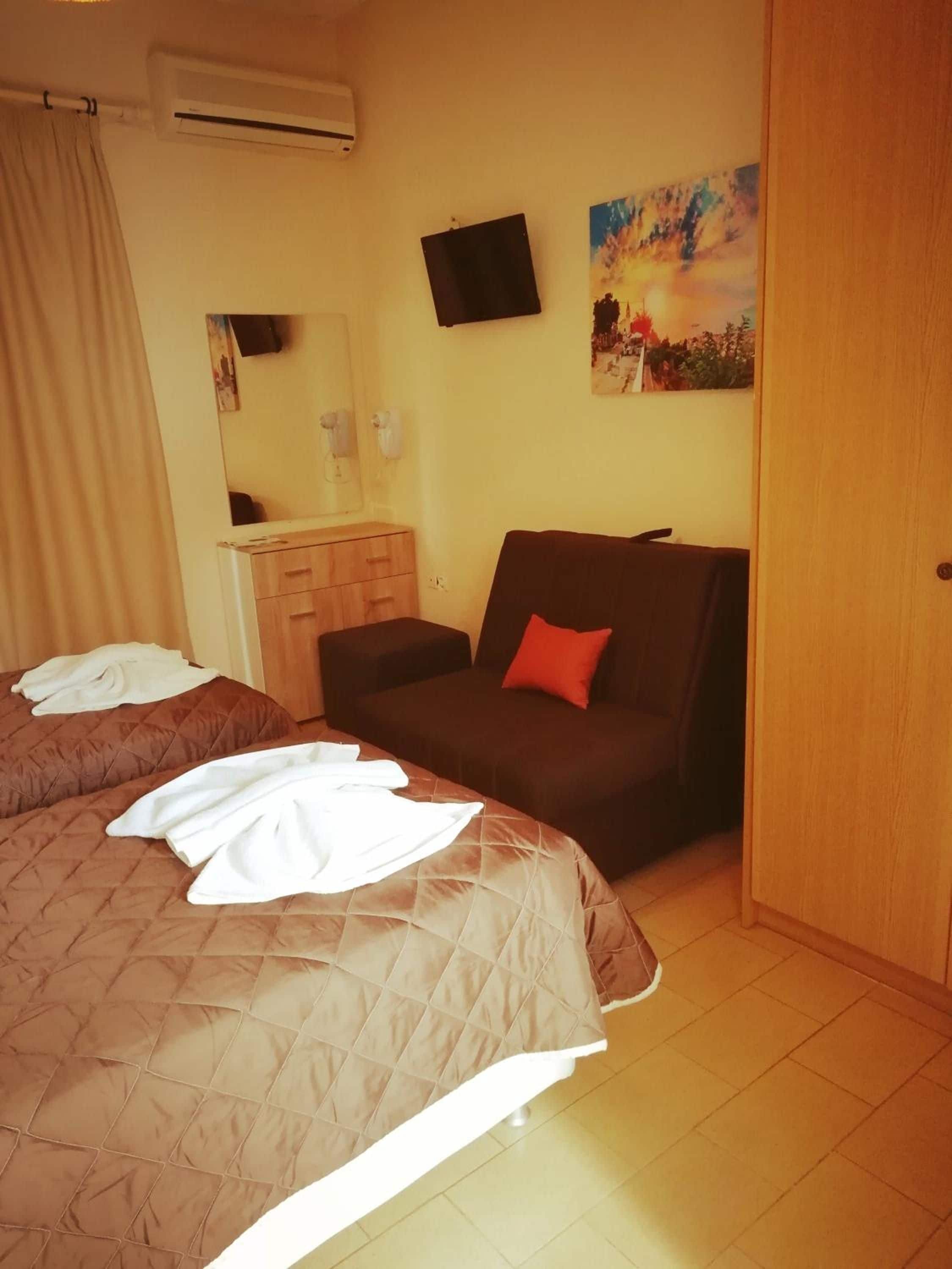Una camera d'albergo con un letto, una sedia, un armadio, uno specchio e un quadro appeso al muro.