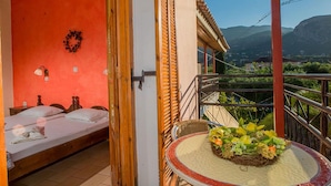 Quarto com cama, mesa com um arranjo floral e varanda com vista para montanhas.