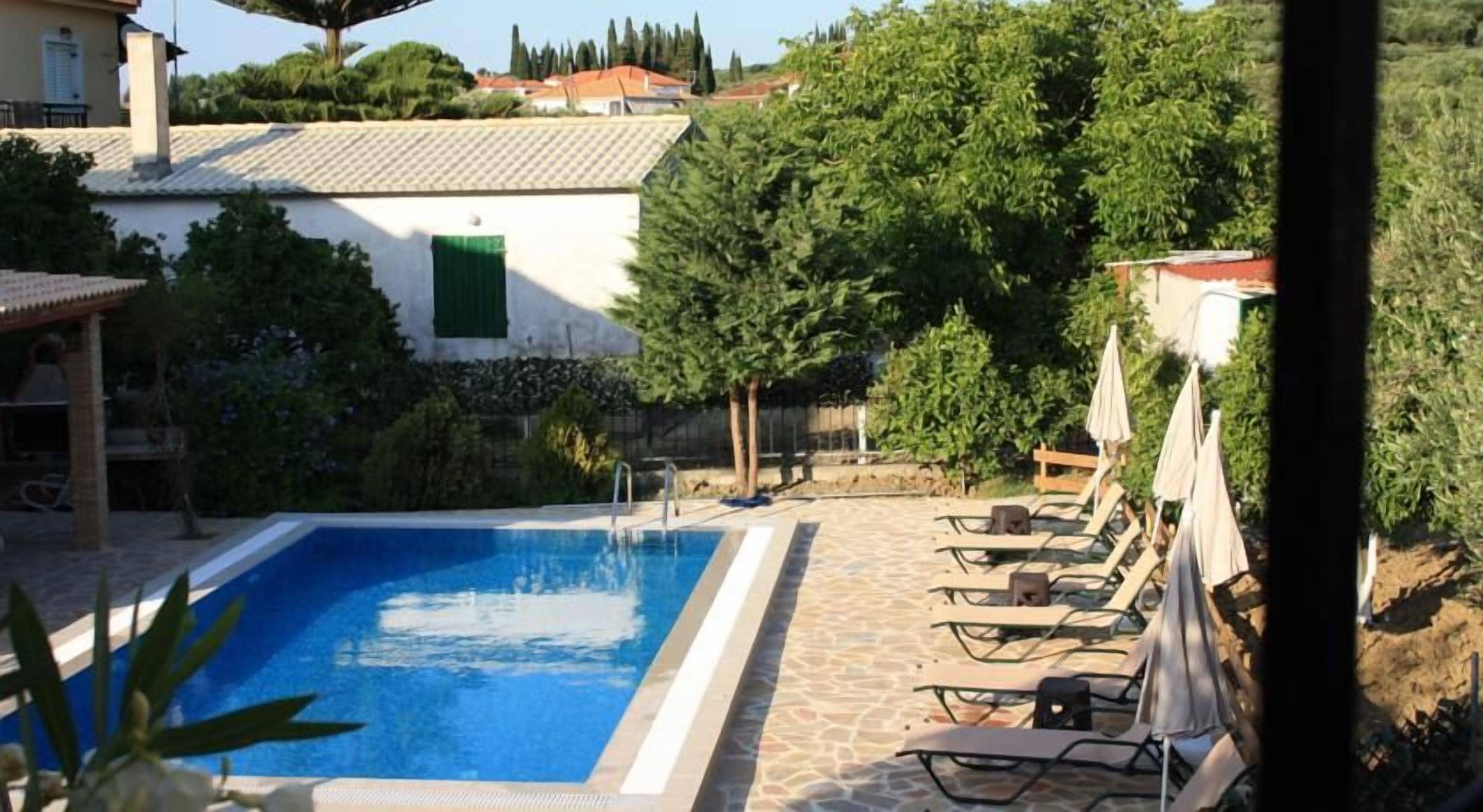 Ein Pool mit Liegestühlen und Sonnenschirmen, umgeben von Grünflächen und einem Gebäude mit Ziegeldach.