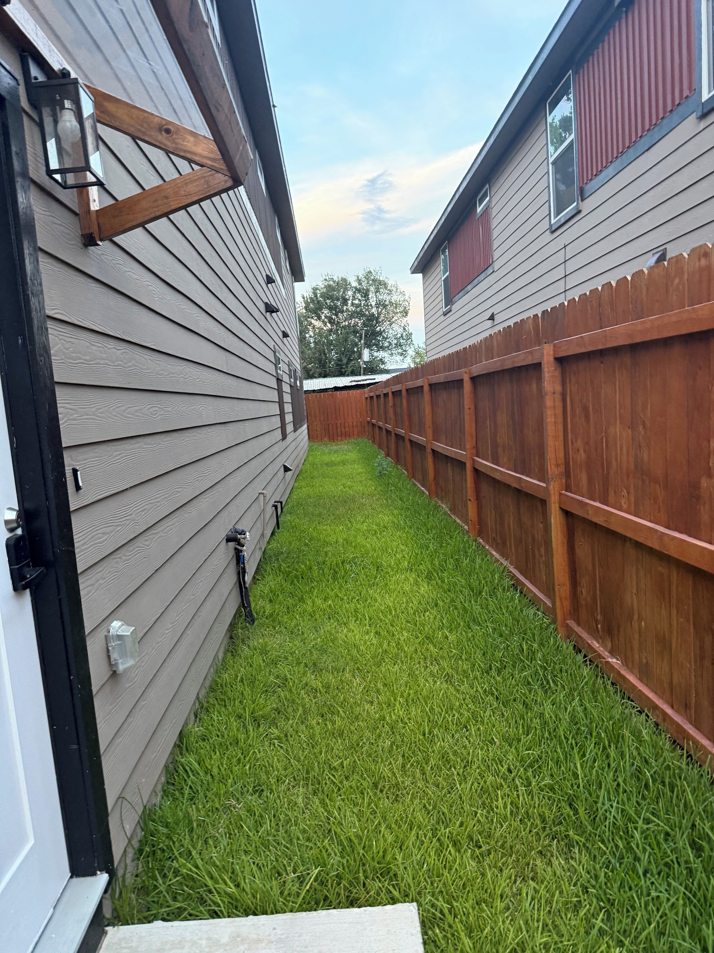 A backyard with a wooden fence, a grassy lawn, and a house with siding.