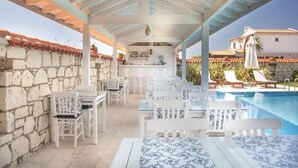 Zona d'estar exterior coberta amb mobiliari blanc i una piscina.
