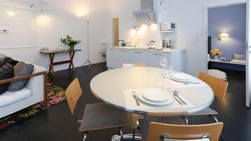 Un comedor moderno con una mesa redonda para dos personas, un sofá blanco y una cocina al fondo.