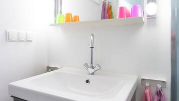 Un baño con un lavamanos blanco, un espejo con luces y tazas de colores en una estantería.