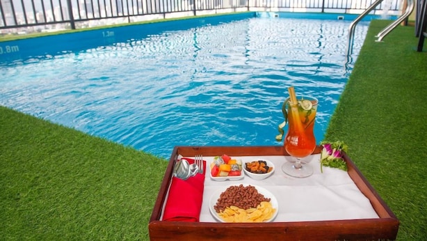 A poolside dining setup with a tray containing a drink, snacks, and a salad. - Gemma Hotel (Da Nang Municipality)