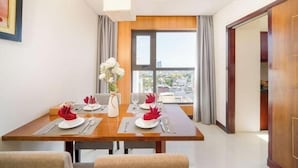A dining area with a table set for two, a vase with flowers, and a window with curtains. - Gemma Hotel (Da Nang Municipality)