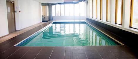 Una piscina interior con suelo de baldosas, techo transparente y ventanas a lo largo de una pared.
