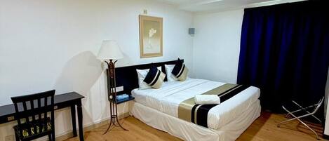 A room with a bed, a desk, a chair, a lamp, and a curtain.