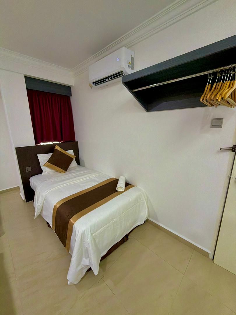 A hotel room with a bed, a wardrobe, a red curtain, and a ceiling-mounted air conditioning unit.