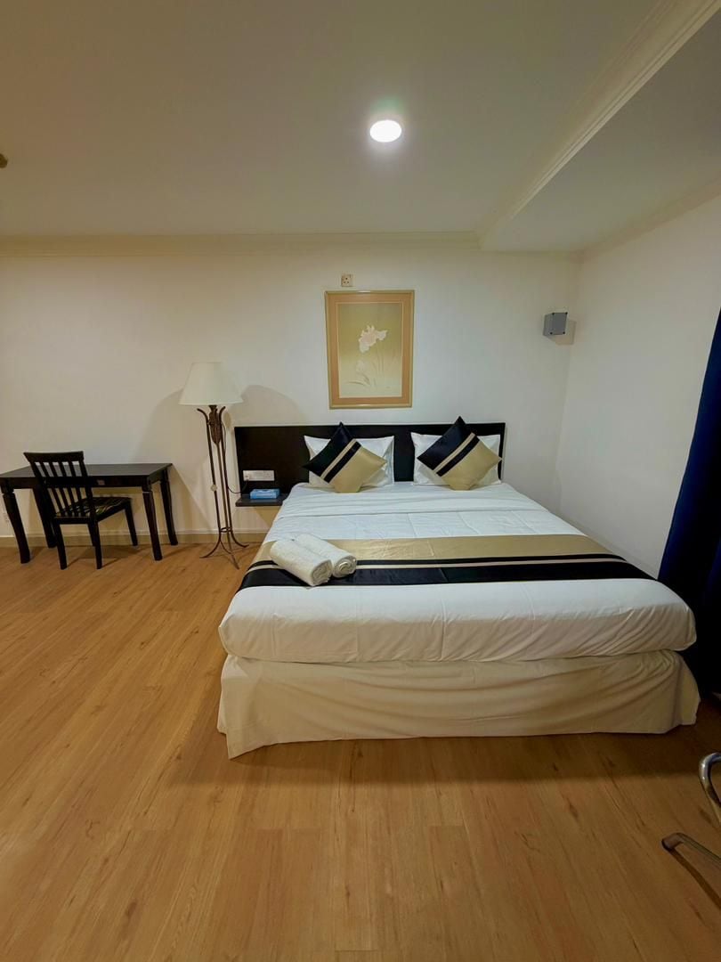 A hotel room with a bed, a desk, a chair, and a floor lamp.