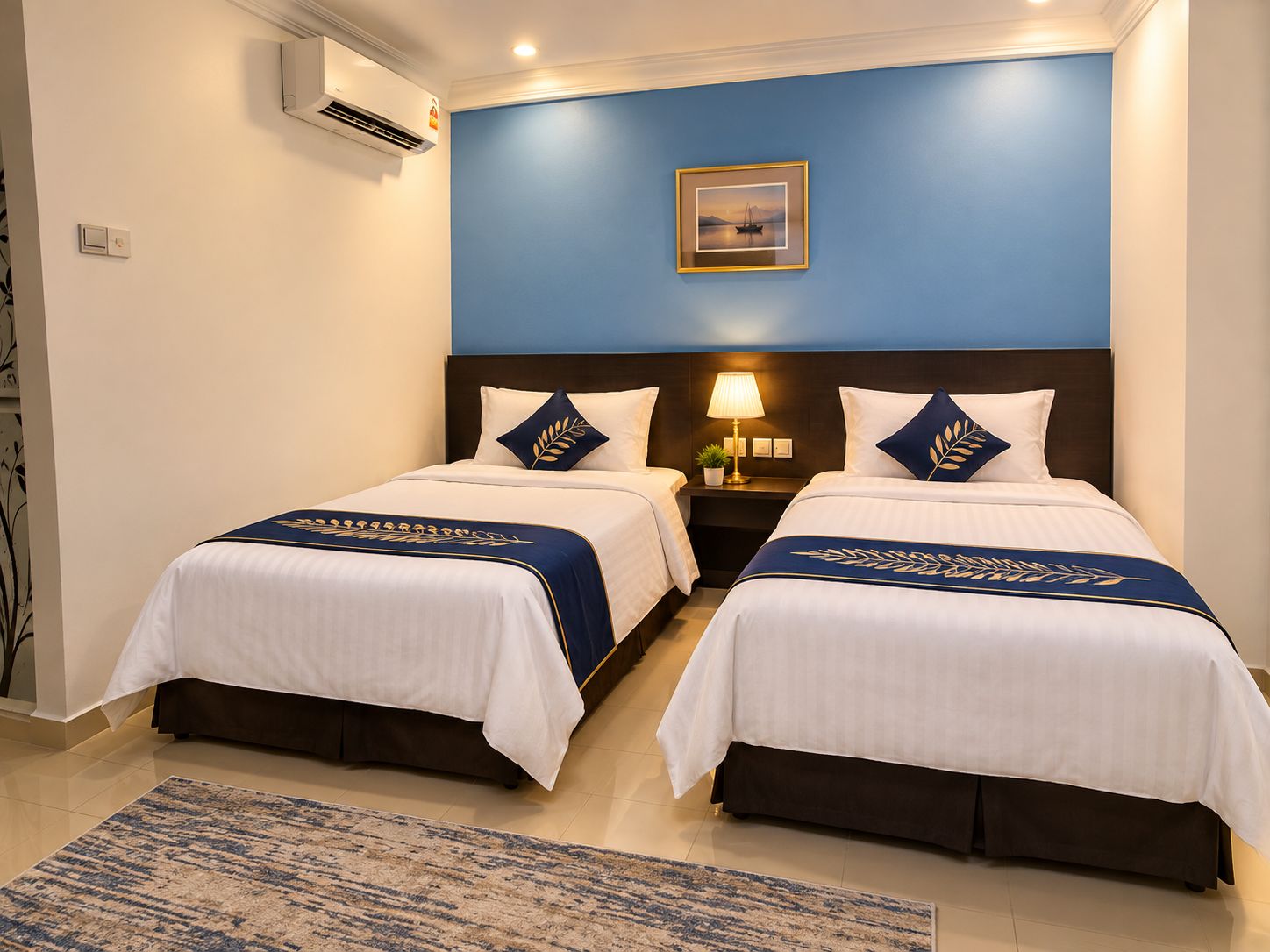 Habitación de hotel con dos camas, una mesita de noche con lámpara, un cuadro en la pared y una pared de acento azul.