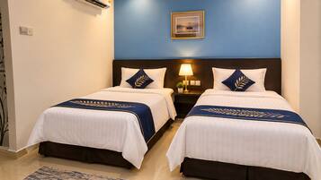 Habitación de hotel con dos camas, una mesita de noche con lámpara, un cuadro en la pared y una pared de acento azul.