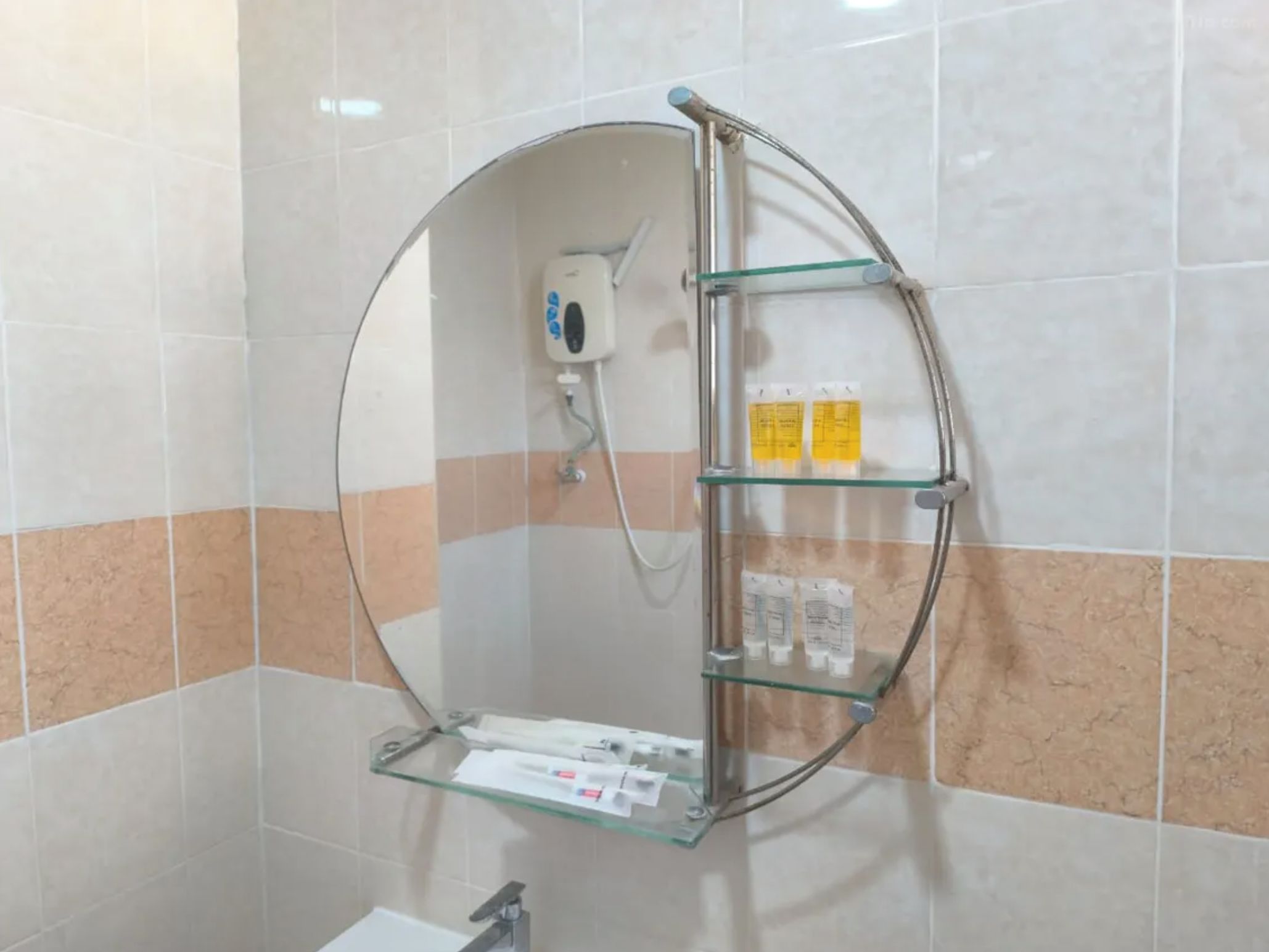 A bathroom with a circular mirror, a handheld showerhead, and a glass shelf with toiletries.