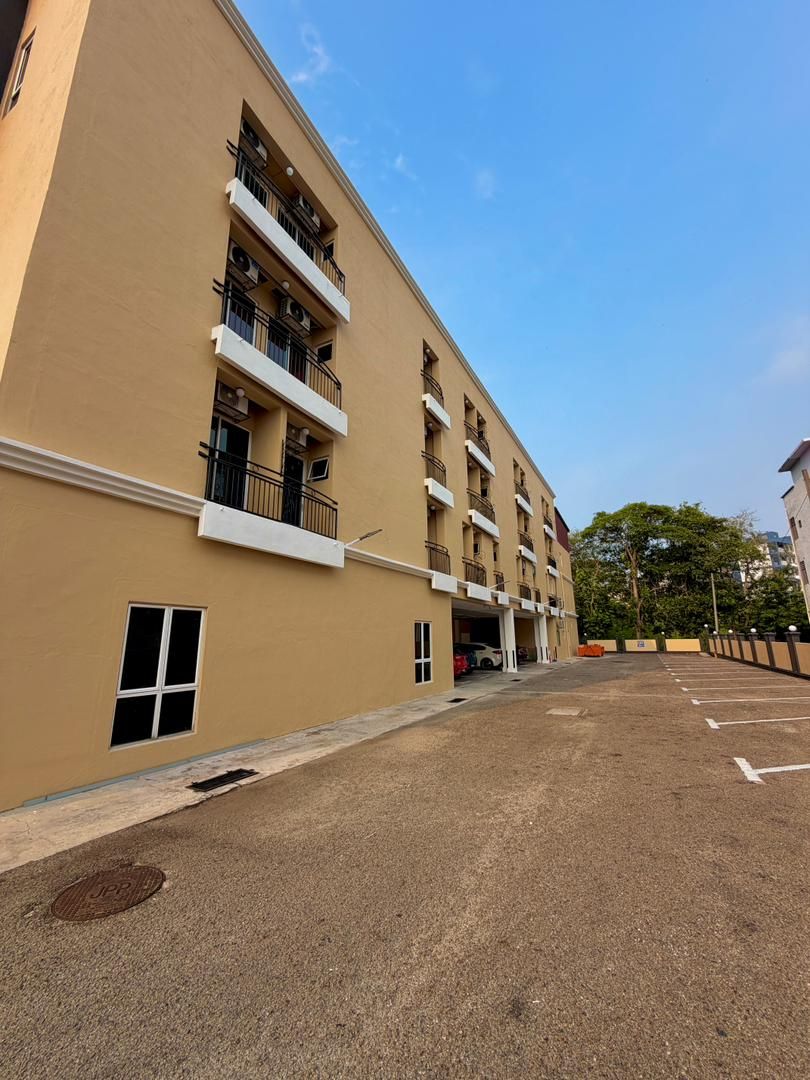 A multi-story building with balconies, a parking lot, and a clear sky.