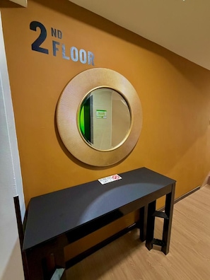 Pasillo del segundo piso con un espejo redondo en la pared, un banco negro y un cartel de 'No Fumar'.